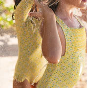 Two women standing close together outdoors, one wearing a yellow dress and the other in a patterned top.