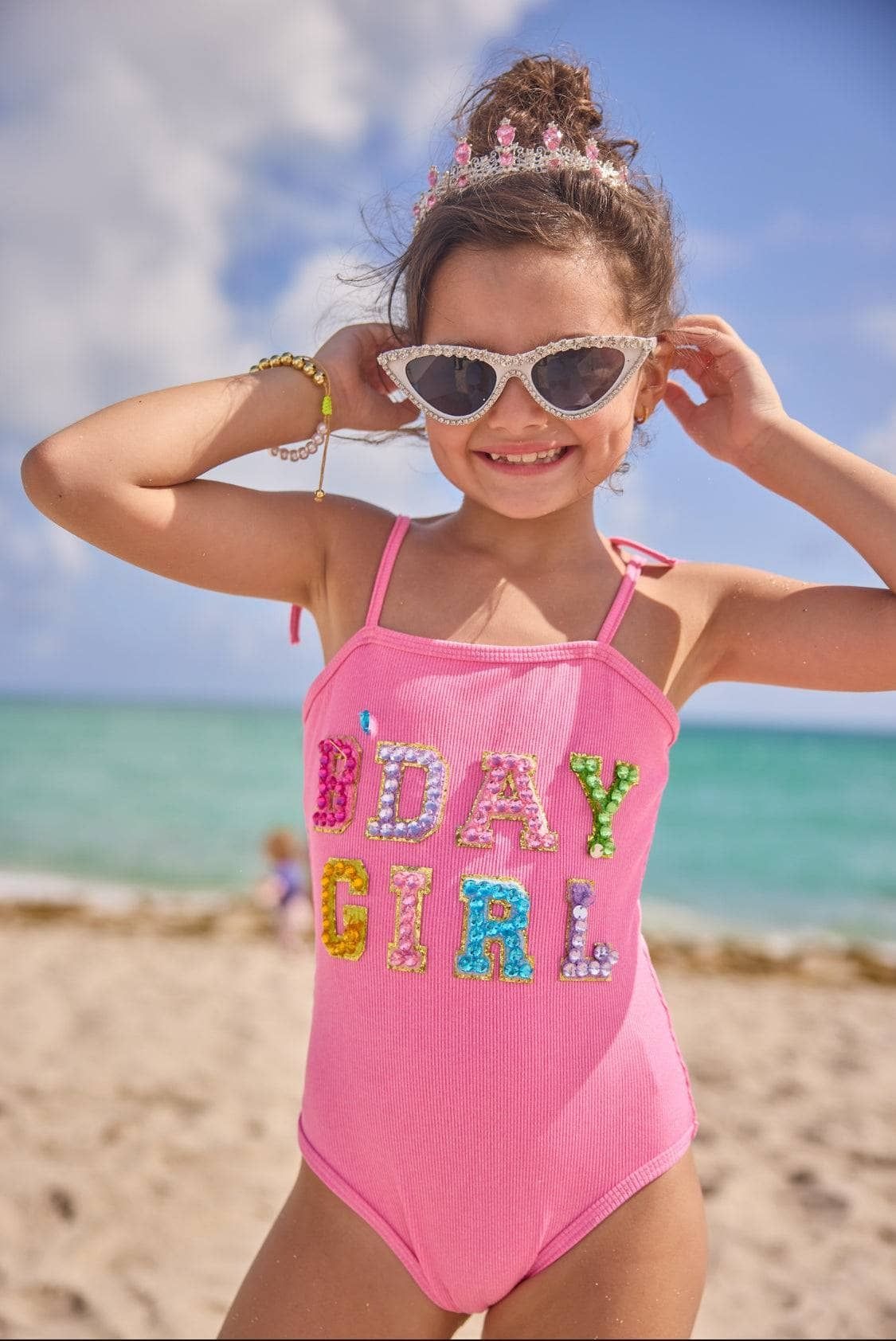 Young girl in a pink swimsuit with colorful letters on a beach