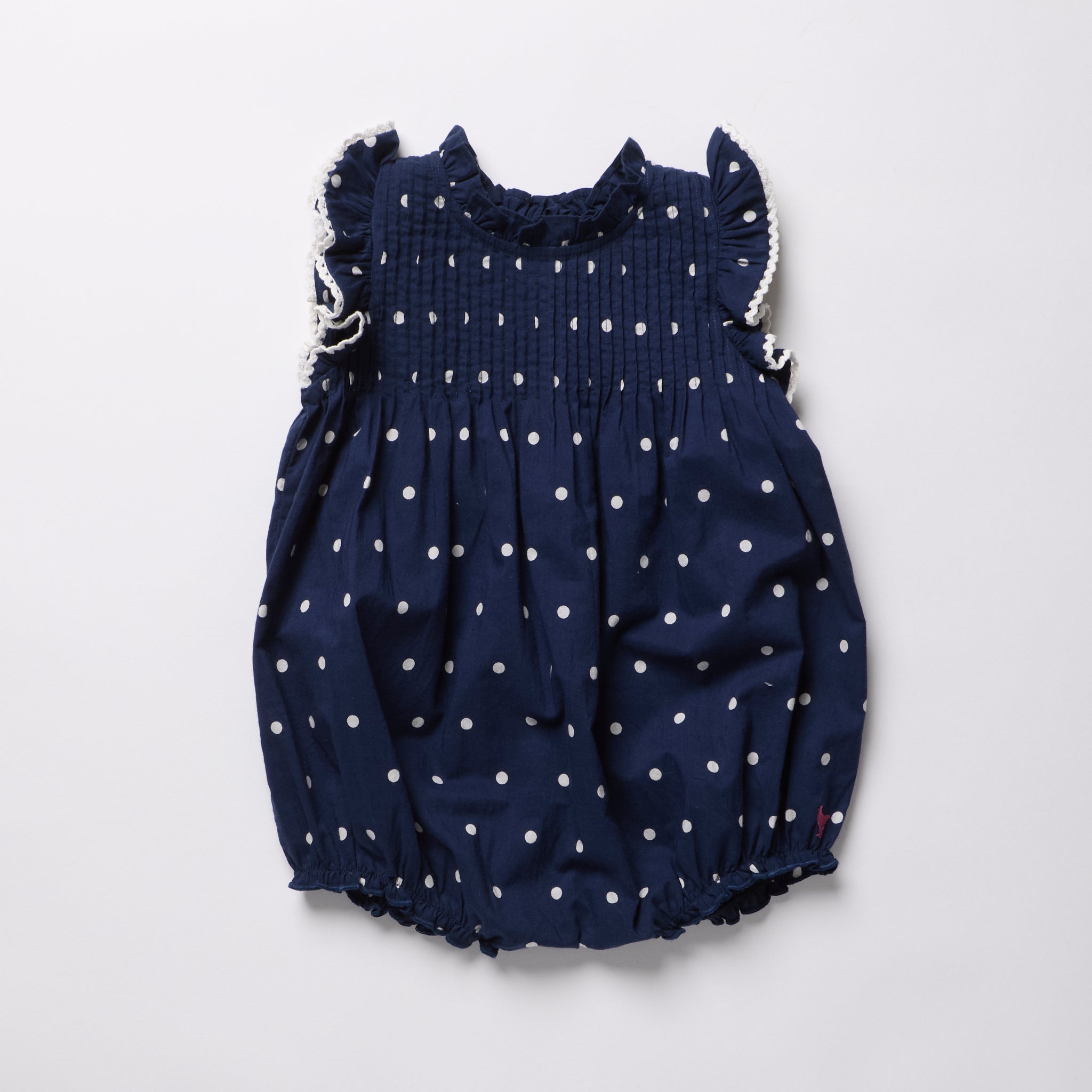 Navy blue romper with white polka dots on a light gray background