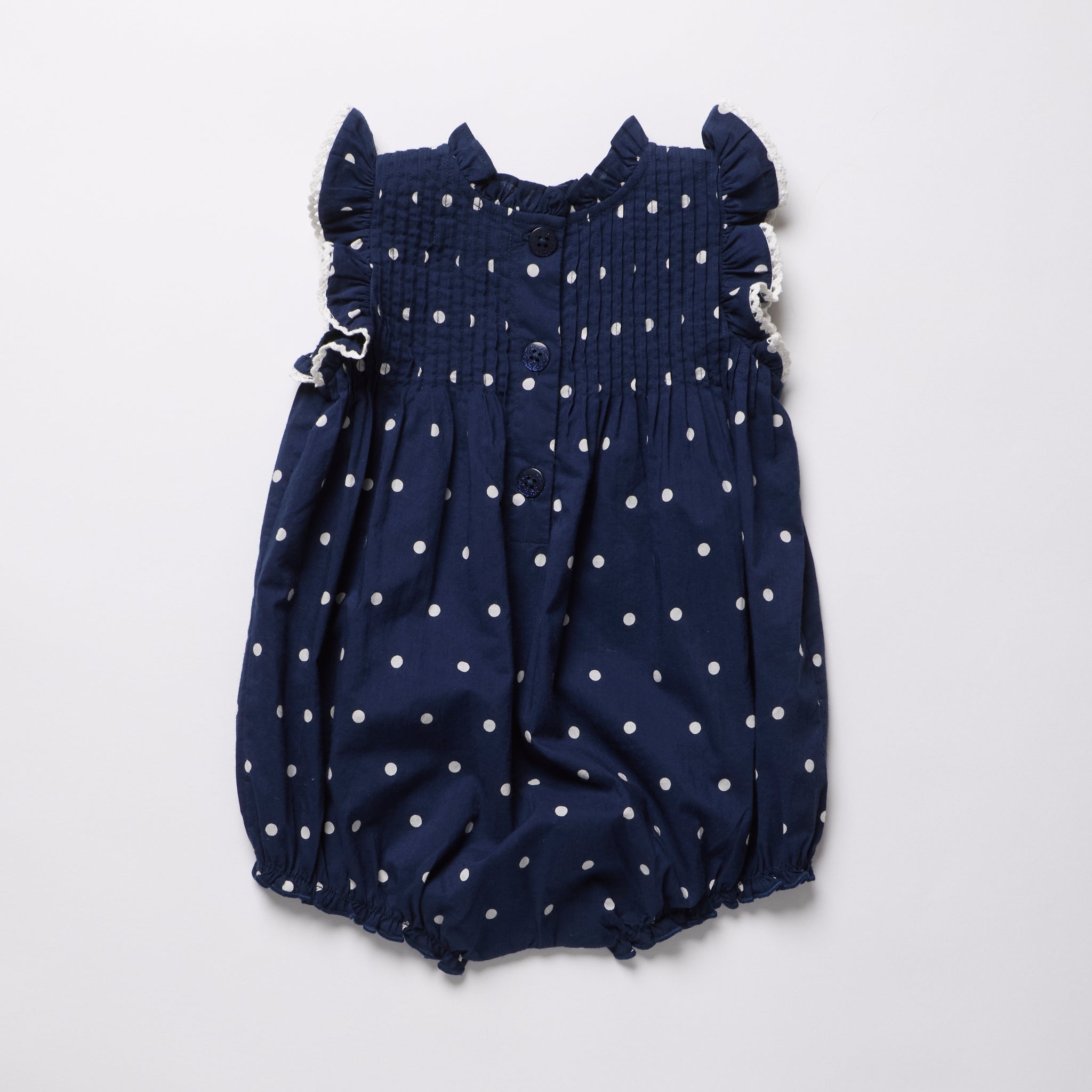 Navy blue romper with white polka dots on a light gray background