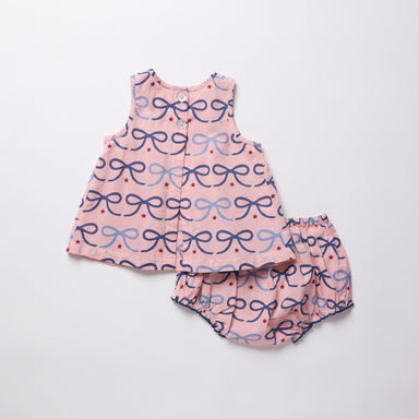 Baby dress and bloomers set with bow pattern on a light gray background