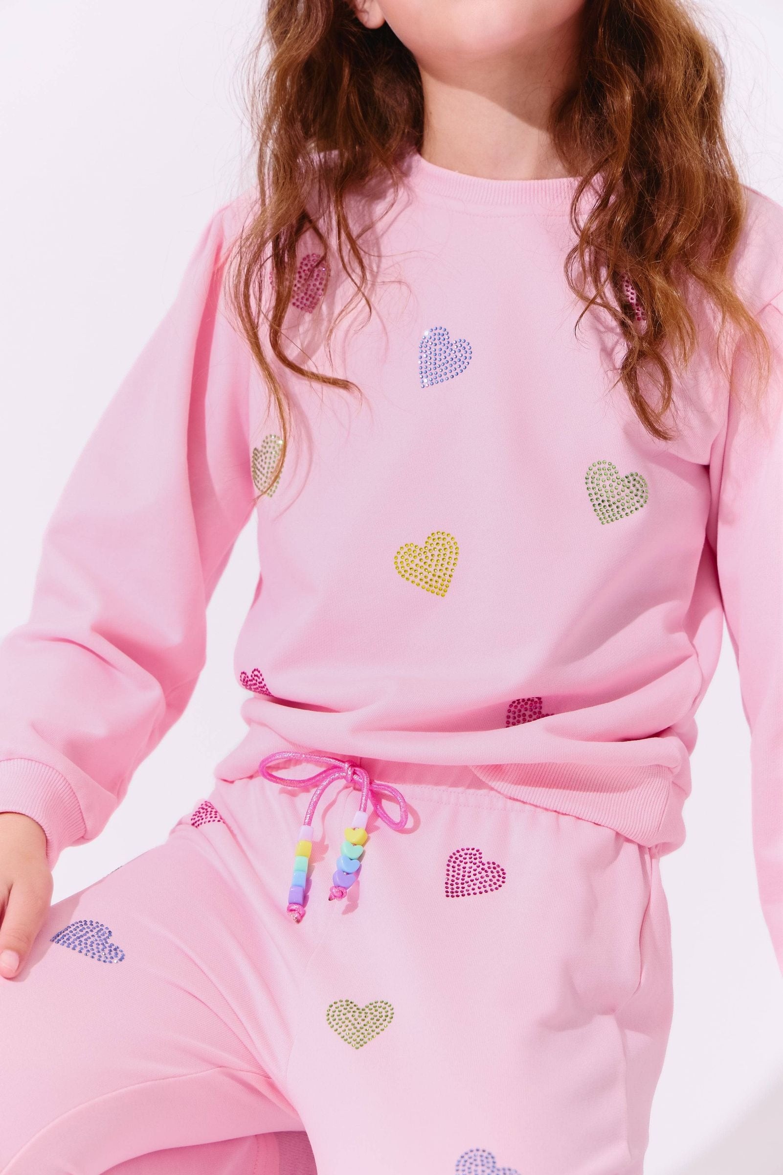Child wearing a pink outfit with heart patterns on a white background