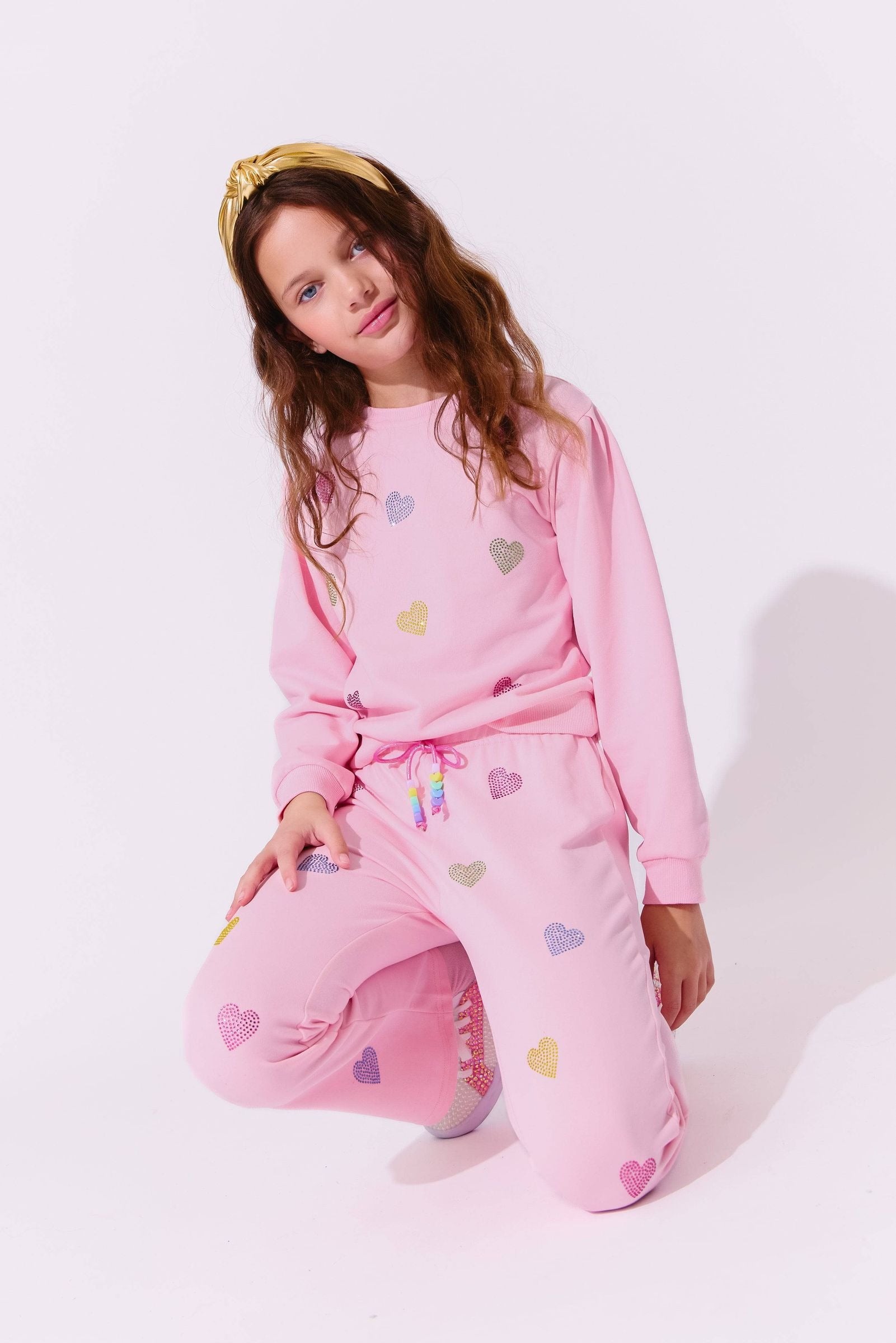 Young girl wearing pink sweatsuit with heart patterns on a white background
