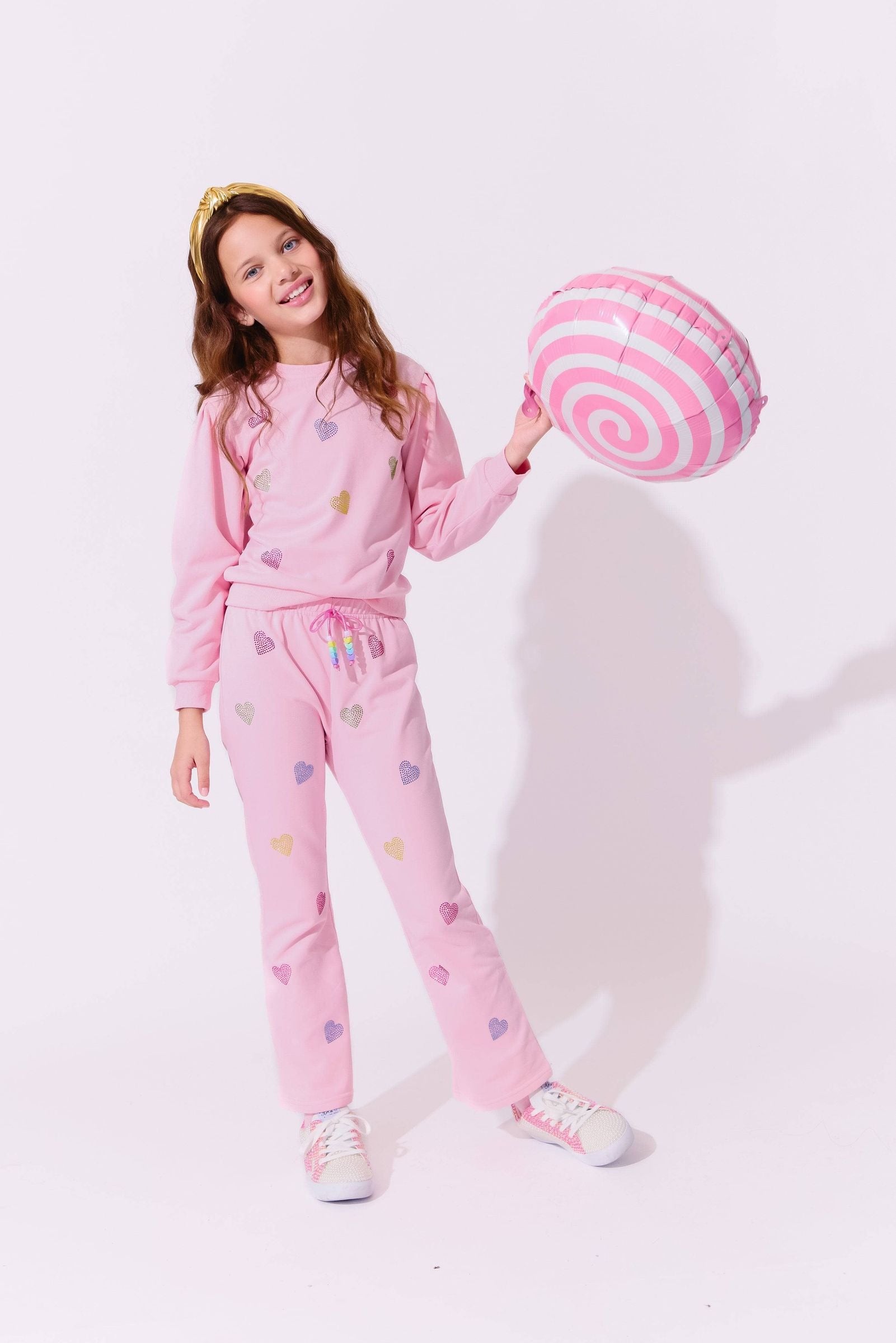 Young girl in pink outfit holding a pink and white striped ball against a white background