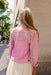 Person wearing a pink jacket with beaded details, standing against a beige wall.