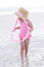 Child in a pink swimsuit and straw hat with ribbon on a beach