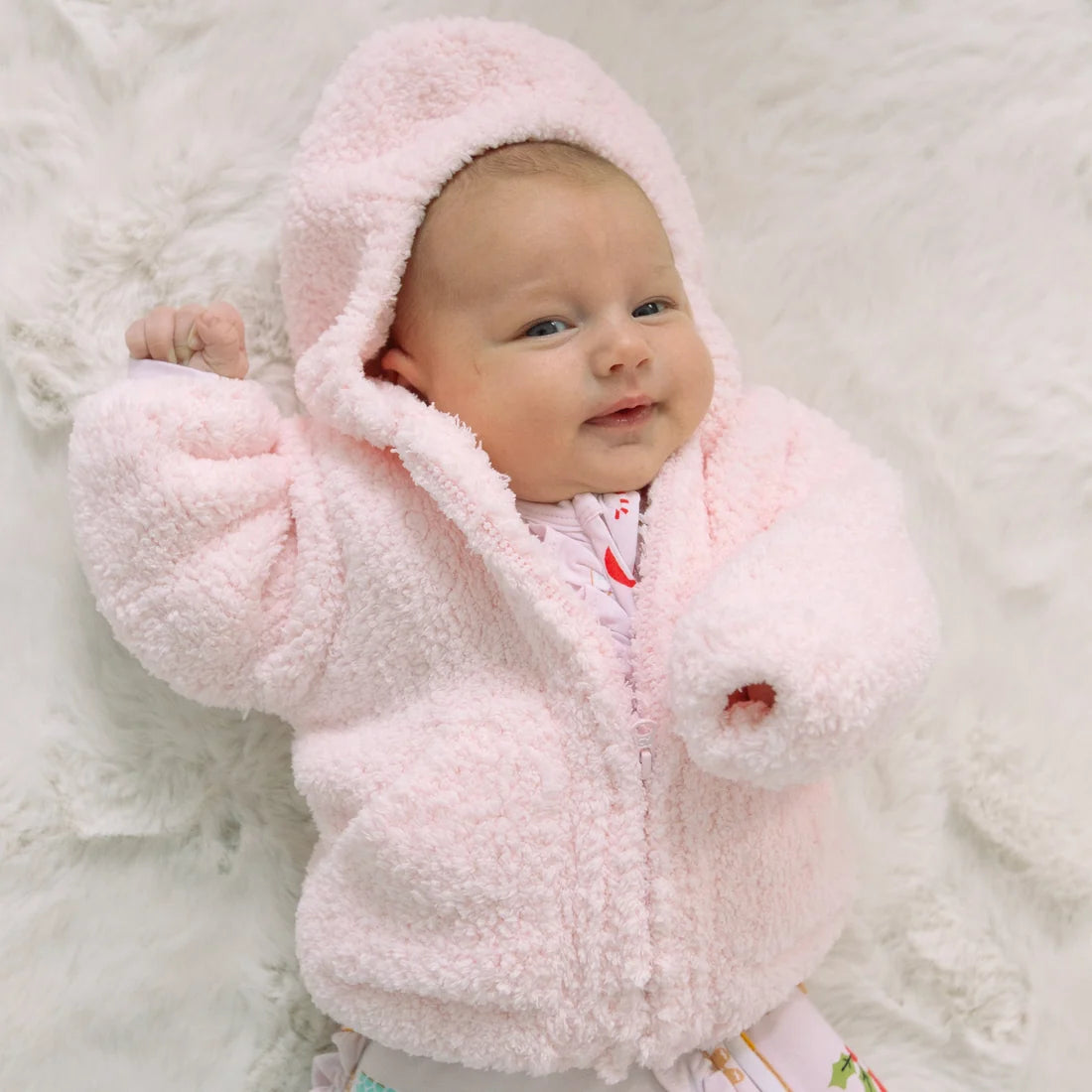 Baby wearing a soft pink chenille hooded jacket while lying on a white fluffy blanket Angel Dear cozy outerwear for chilly days