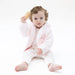 Baby wearing a soft pink chenille hoodie and patterned outfit while sitting barefoot on a white background. Angel Dear outerwear for cozy everyday wear.