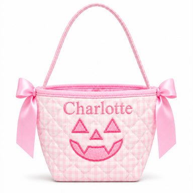 A pink gingham quilted mini bucket bag with a pink satin handle, bow details on the sides, and an embroidered jack-o'-lantern face and the name 'Charlotte' on the front.