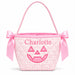 A pink gingham quilted mini bucket bag with a pink satin handle, bow details on the sides, and an embroidered jack-o'-lantern face and the name 'Charlotte' on the front.