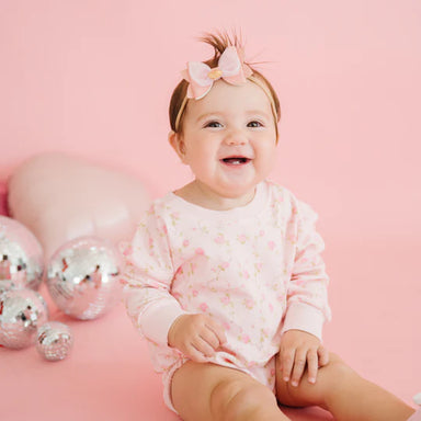 Baby in a pink outfit with a bow sitting on a pink surface with disco balls.