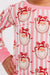 A close up of a children's pajama set featuring a pink and white striped pattern with cartoon santa faces wearing red bows, complete with solid pink cuffs and collar.