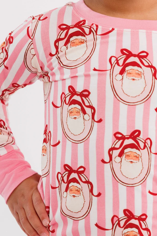 A close up of a children's pajama set featuring a pink and white striped pattern with cartoon santa faces wearing red bows, complete with solid pink cuffs and collar.