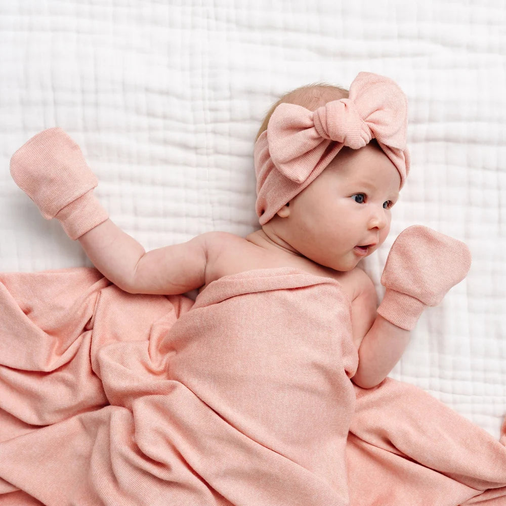 Baby in pink outfit with a large bow headband on a white textured background