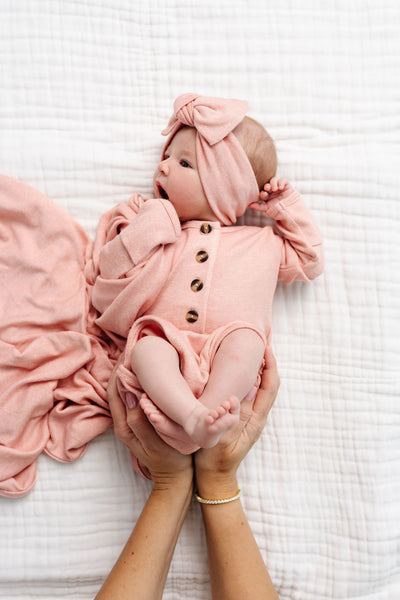 Newborn baby in a pink outfit being held on a white blanket