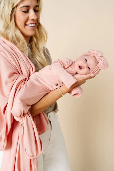 Newborn baby in a pink outfit being held in a woman's arms
