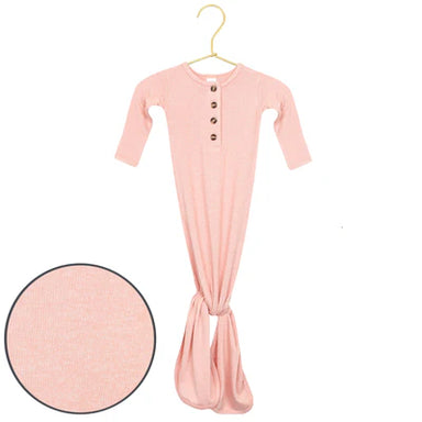 A baby sleep sack in light pink with a small button placket, hanging on a gold hanger against a white background, with a circular fabric texture inset in the lower left corner.