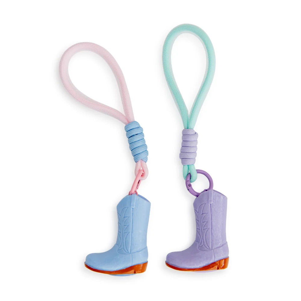 Two cowboy boot lip balm keychains on a white background. One keychain has a pink loop and a light blue boot with an orange sole, and the other has a mint green loop and a lavender boot with an orange sole.