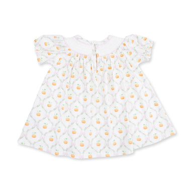 A white baby smocked dress with short flutter sleeves, featuring a repeating pattern of orange peaches and green leaves over a light pink trellis design.