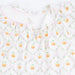 A close-up of a white baby dress featuring a repeating pattern of orange pumpkins, green vines, and pink bows, with a smocked neckline.