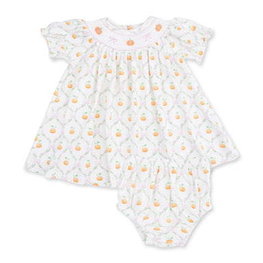 A baby dress set in white fabric, featuring a repeating pattern of orange pumpkins, green leaves, and a light pink trellis design. The dress has ruffled short sleeves and a smocked neckline with small embroidered bows.