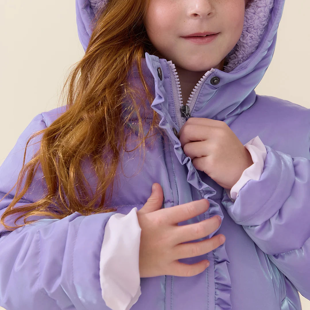 A close-up of a child wearing a lavender hooded puffer jacket with a white inner collar, holding the zipper. The child has long, wavy light brown hair, and the background is a solid light beige.