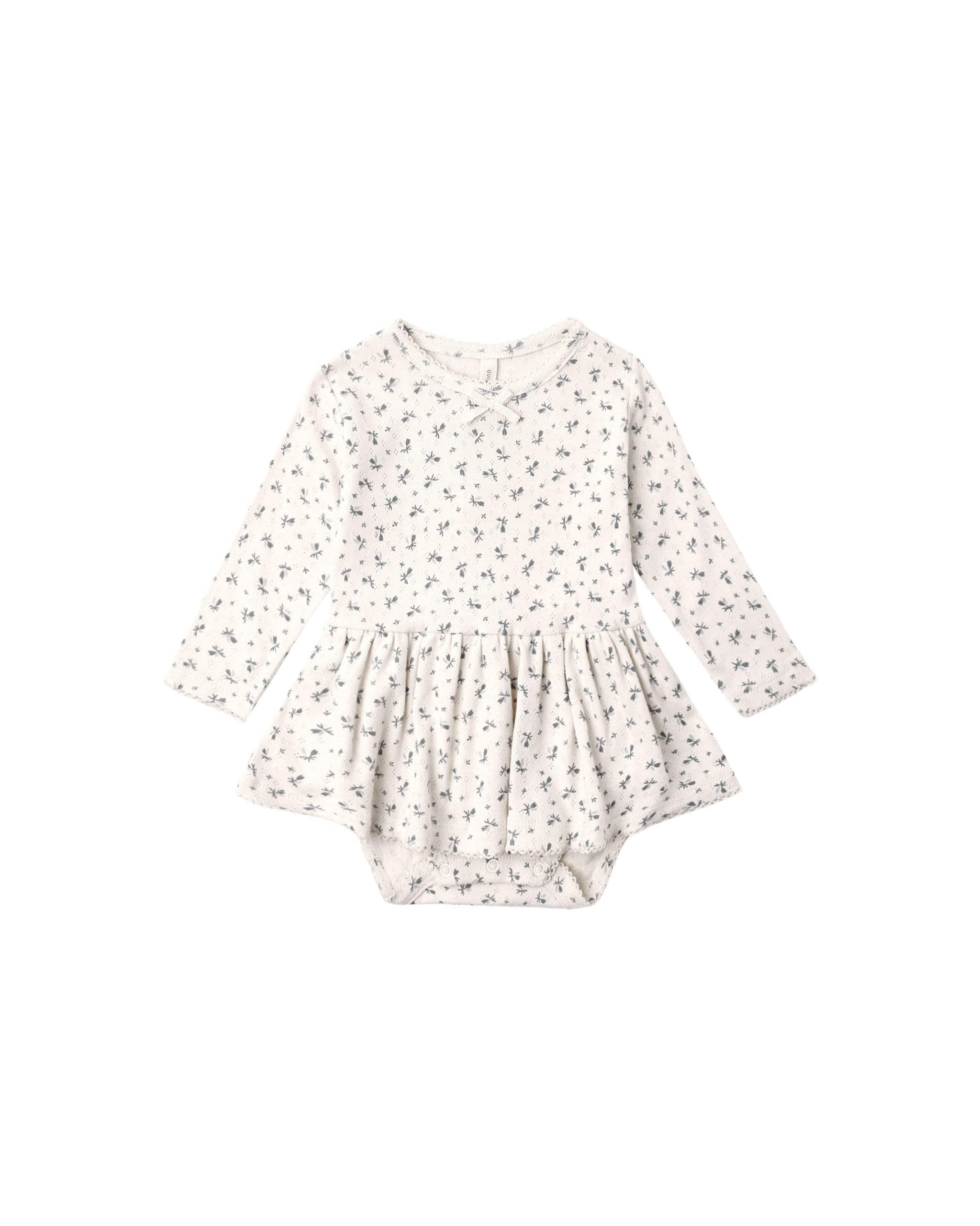 A Pointelle Skirted Bodysuit featuring a peplum skirt, long sleeves, and a delicate bow at the neckline. Designed with snaps at the shoulder and bottom for easy changes.