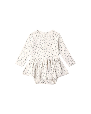 A Pointelle Skirted Bodysuit featuring a peplum skirt, long sleeves, and a delicate bow at the neckline. Designed with snaps at the shoulder and bottom for easy changes.