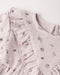 Close-up of a light lilac eyelet fabric garment with ruffled trim and a small floral print, showing the neckline and textured material against a plain light background.