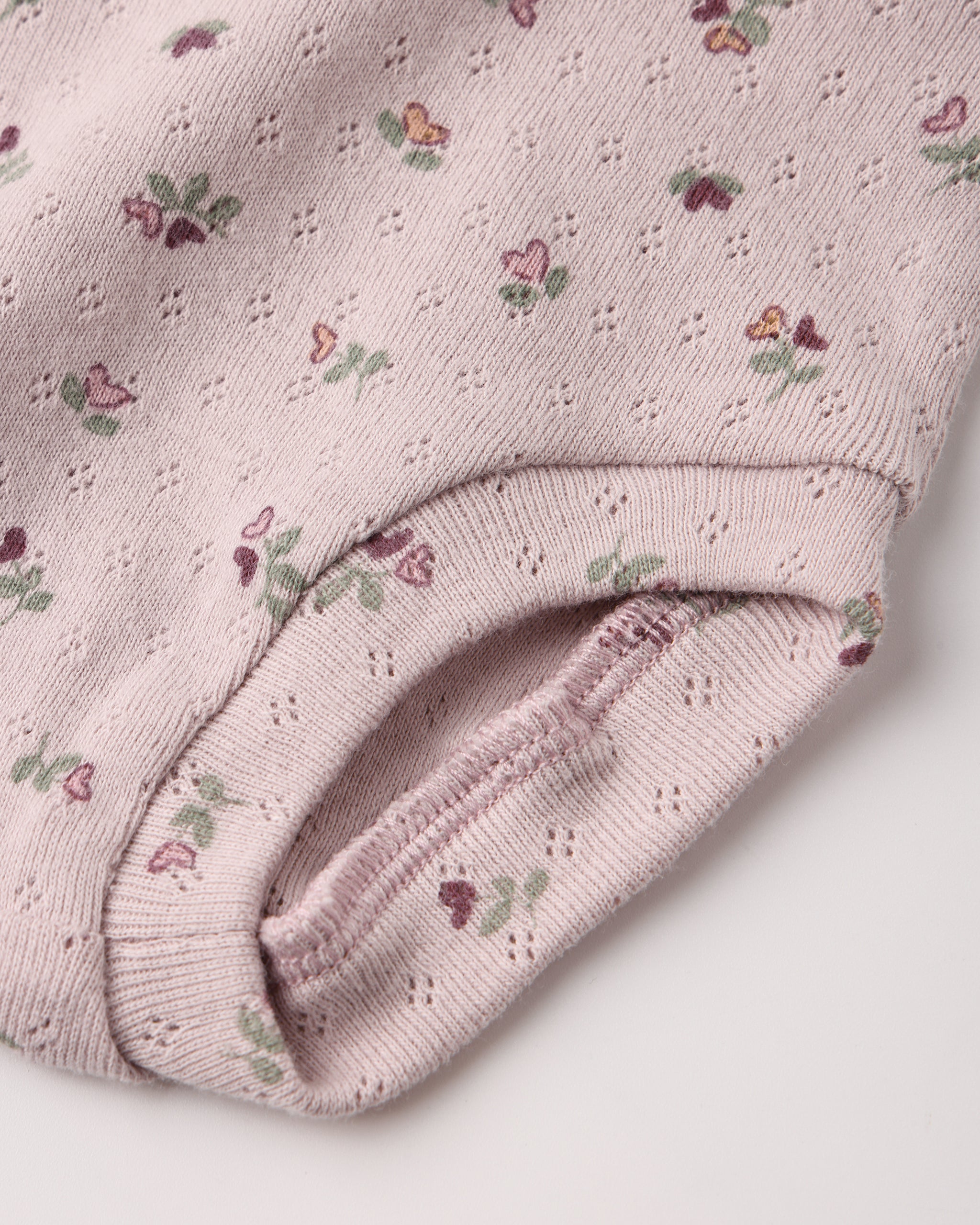 Close-up of a light lilac eyelet fabric diaper cover with a small floral print, showing textured material against a plain light background.