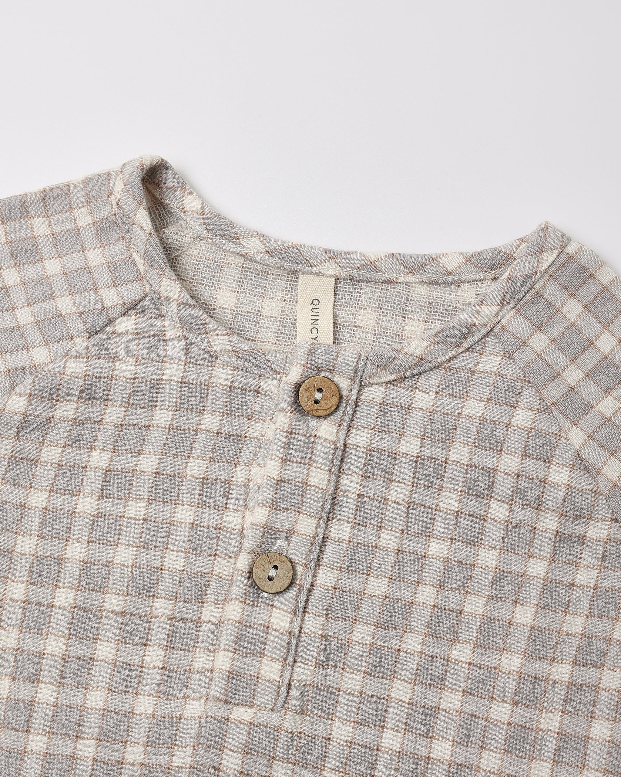 Close-up of a children's long-sleeve henley shirt with a light blue gingham pattern, featuring a button placket with wooden buttons.