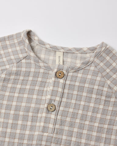 Close-up of a children's long-sleeve henley shirt with a light blue gingham pattern, featuring a button placket with wooden buttons.
