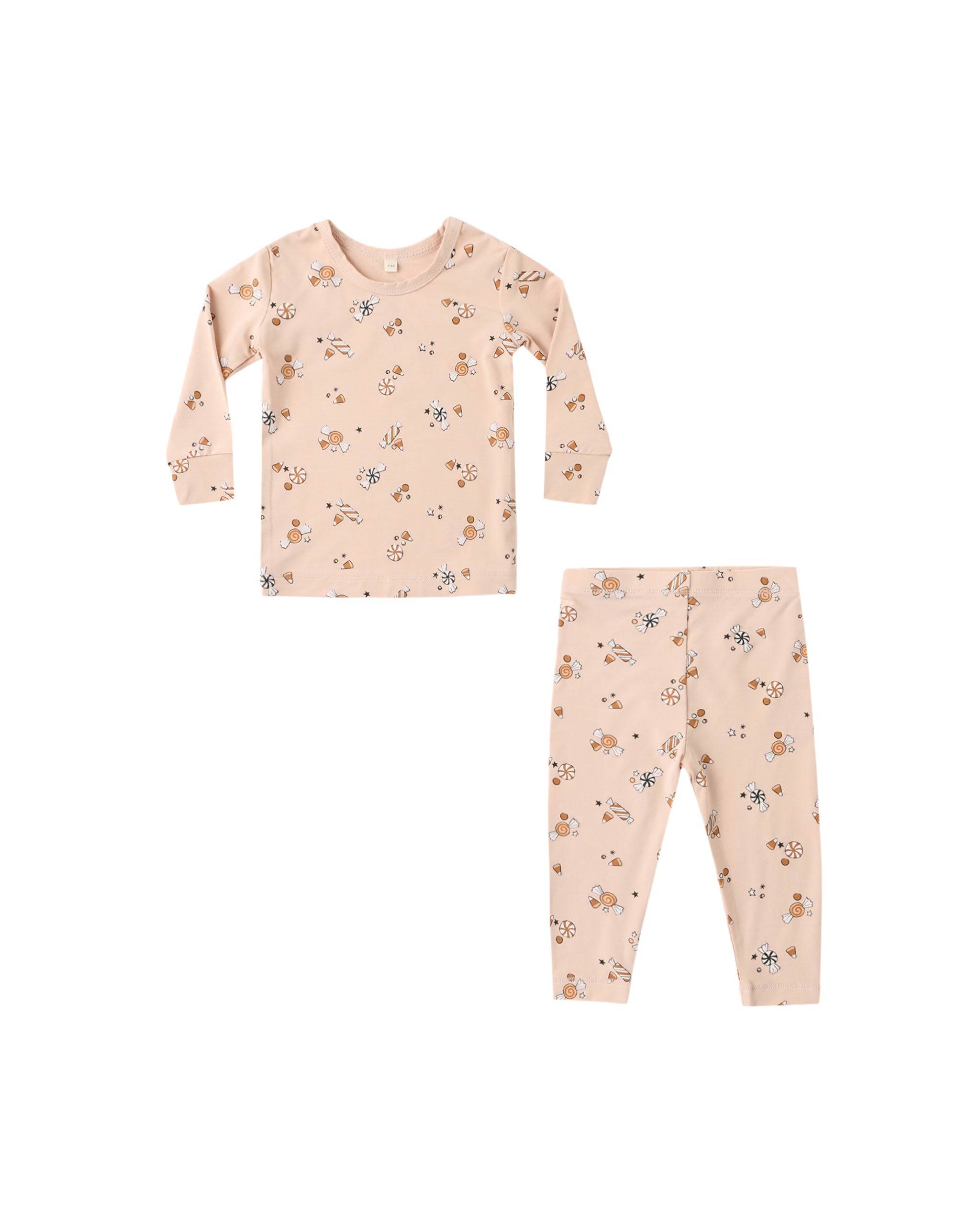 A two-piece children's pajama set featuring a long-sleeve top and matching pants in a warm cream color, both printed with a repeating pattern of small Halloween candy.