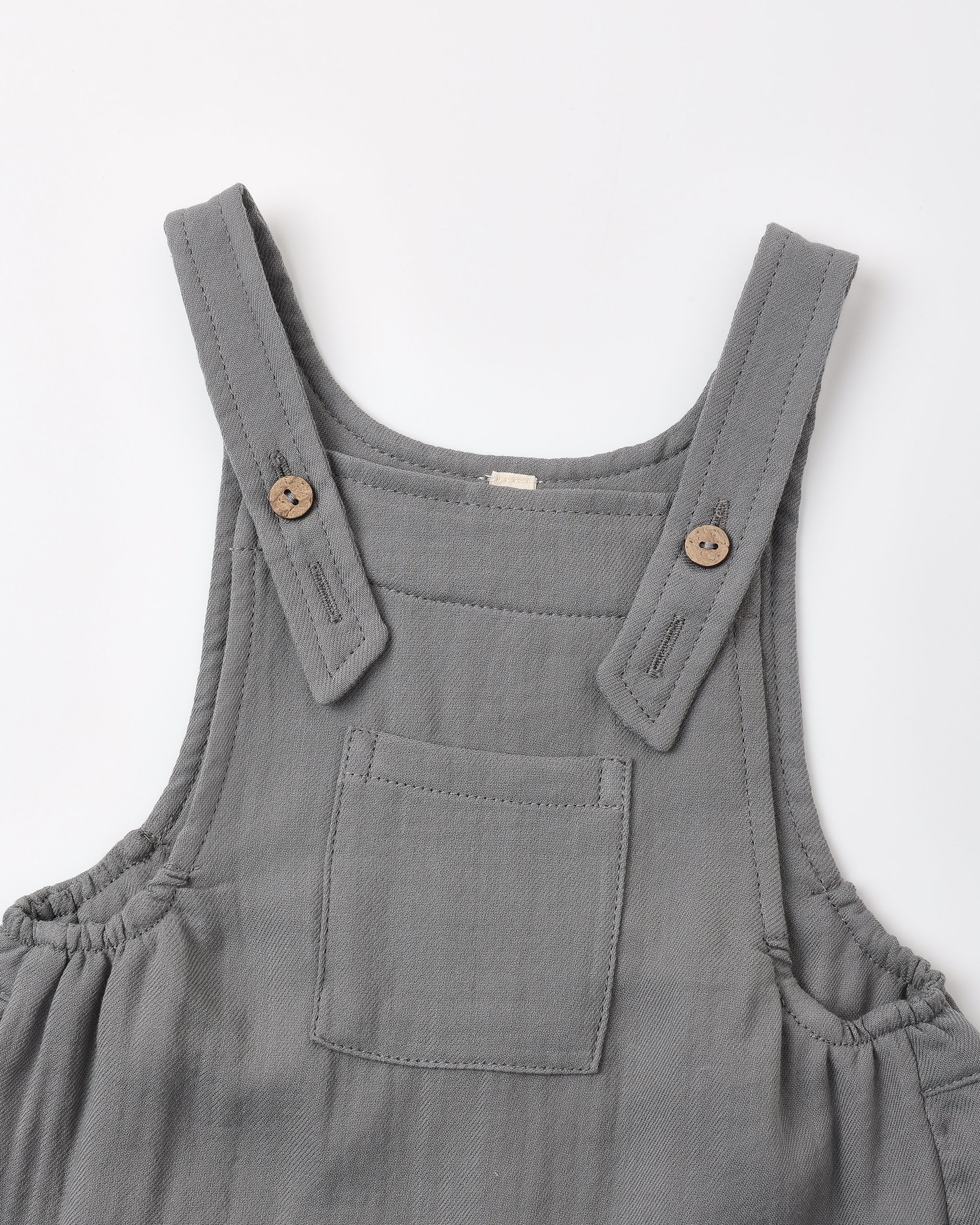 A close-up of a slate overalls with adjustable shoulder straps, decorative wooden buttons, and a front patch pocket, shown on a plain white background.