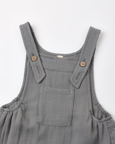A close-up of a slate overalls with adjustable shoulder straps, decorative wooden buttons, and a front patch pocket, shown on a plain white background.