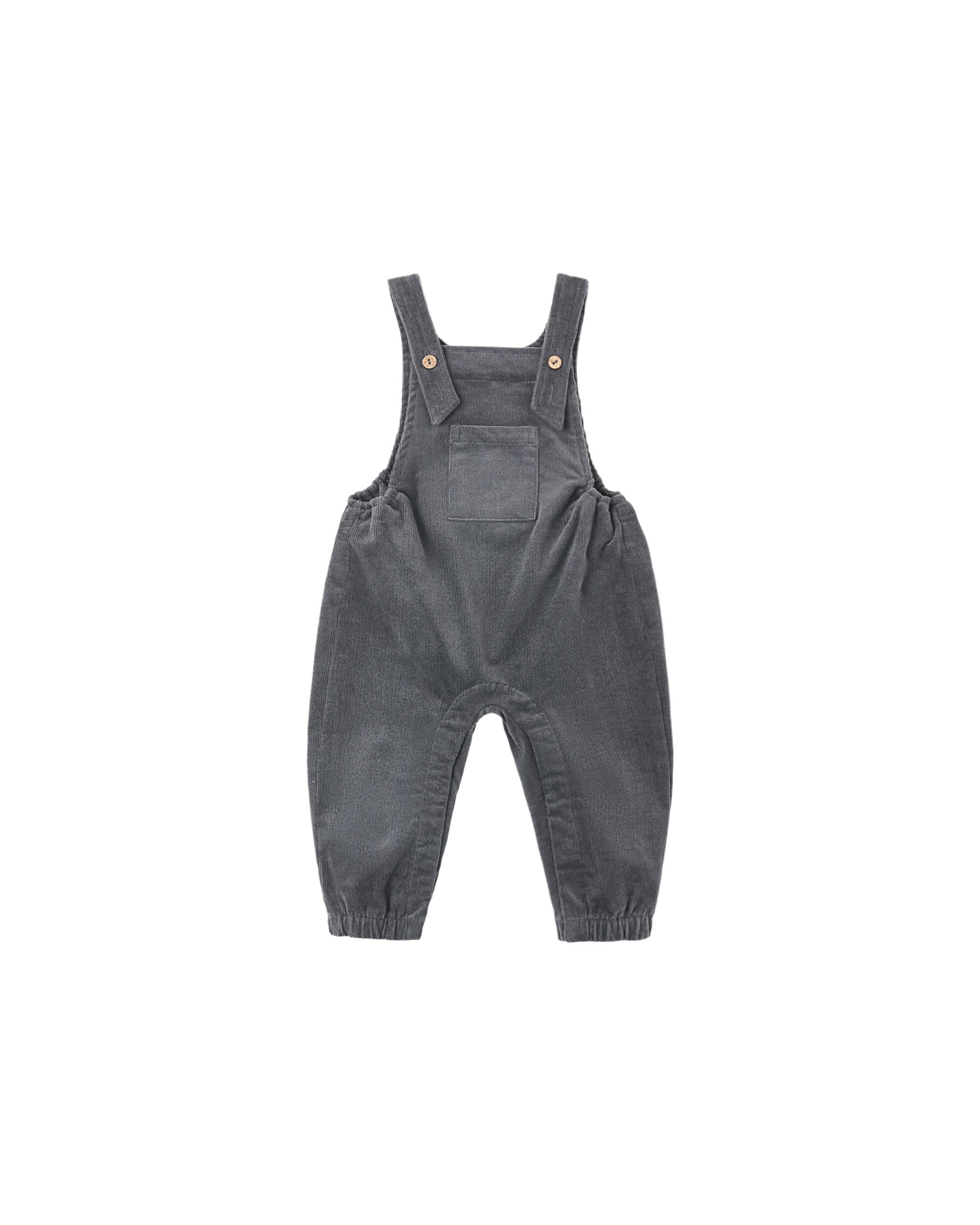 Black overalls adjustable straps and coconut button closures, an open bib pocket, and elastic sides for a comfortable fit. Hidden snaps along the leg inseam (sizes 0–3M to 18–24M) make changes easy.