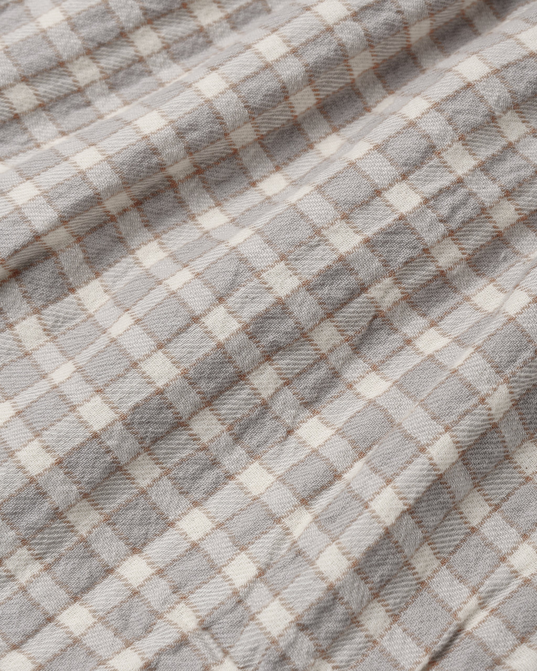 A close-up of a plaid fabric with a gray and off-white checkered pattern and thin brown intersecting lines.