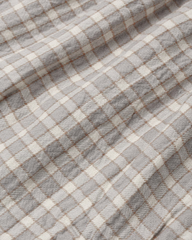 A close-up of a plaid fabric with a gray and off-white checkered pattern and thin brown intersecting lines.