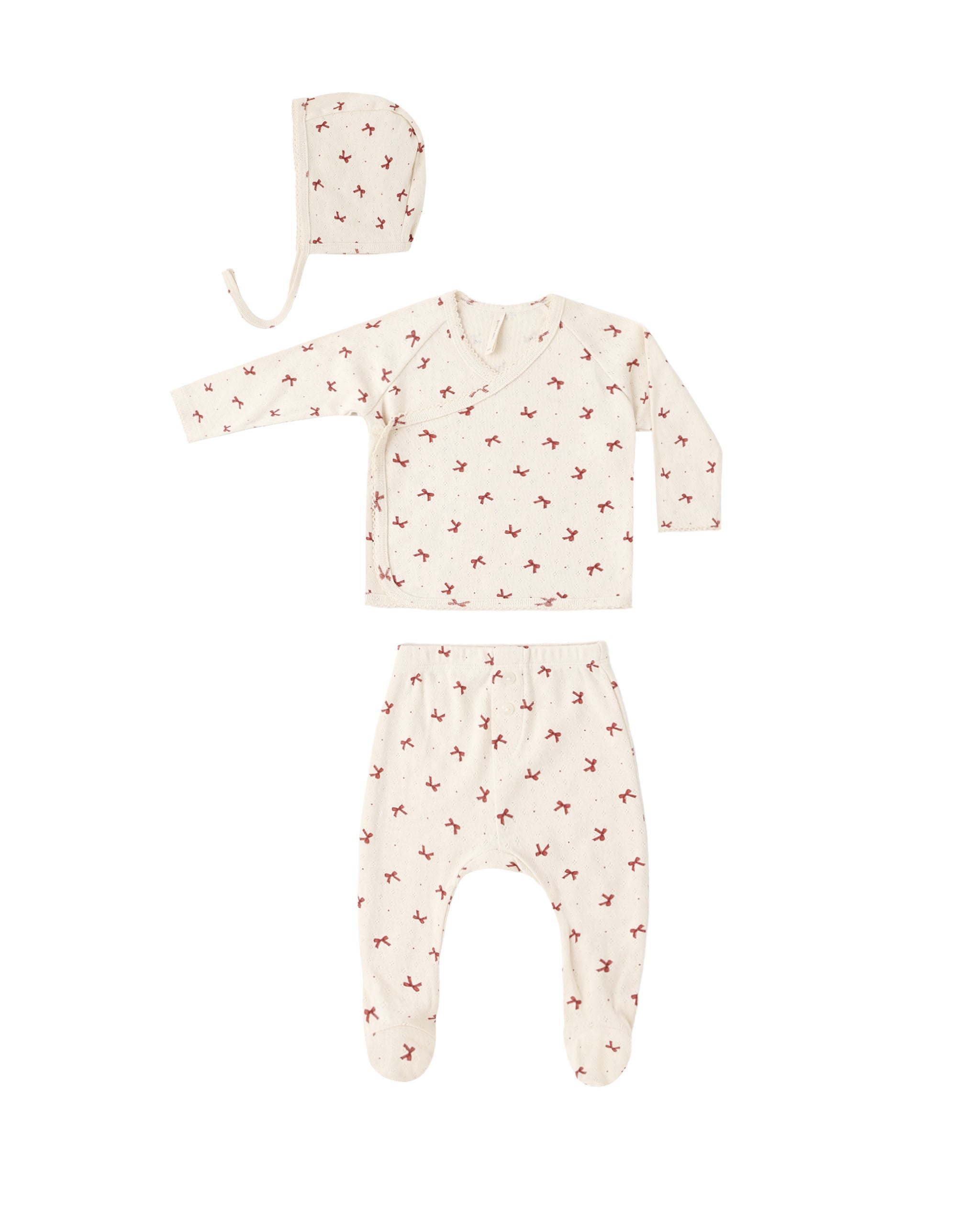 A three-piece baby clothing set laid flat on a white background, including a long-sleeve footed sleeper, matching pants, and a bonnet. The set is cream-colored with a small red dog print pattern.