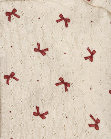 Close-up of a cream-colored knit fabric with a textured eyelet pattern and a repeating motif of small red embroidered bows.