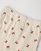 Close-up of cream-colored eyelet fabric with a repeating red bow pattern and two white buttons, photographed on a light neutral background.