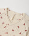 Close-up of a cream-colored knit top with a small red bow pattern and a visible 'Ouincy Mae' brand tag inside the neckline.