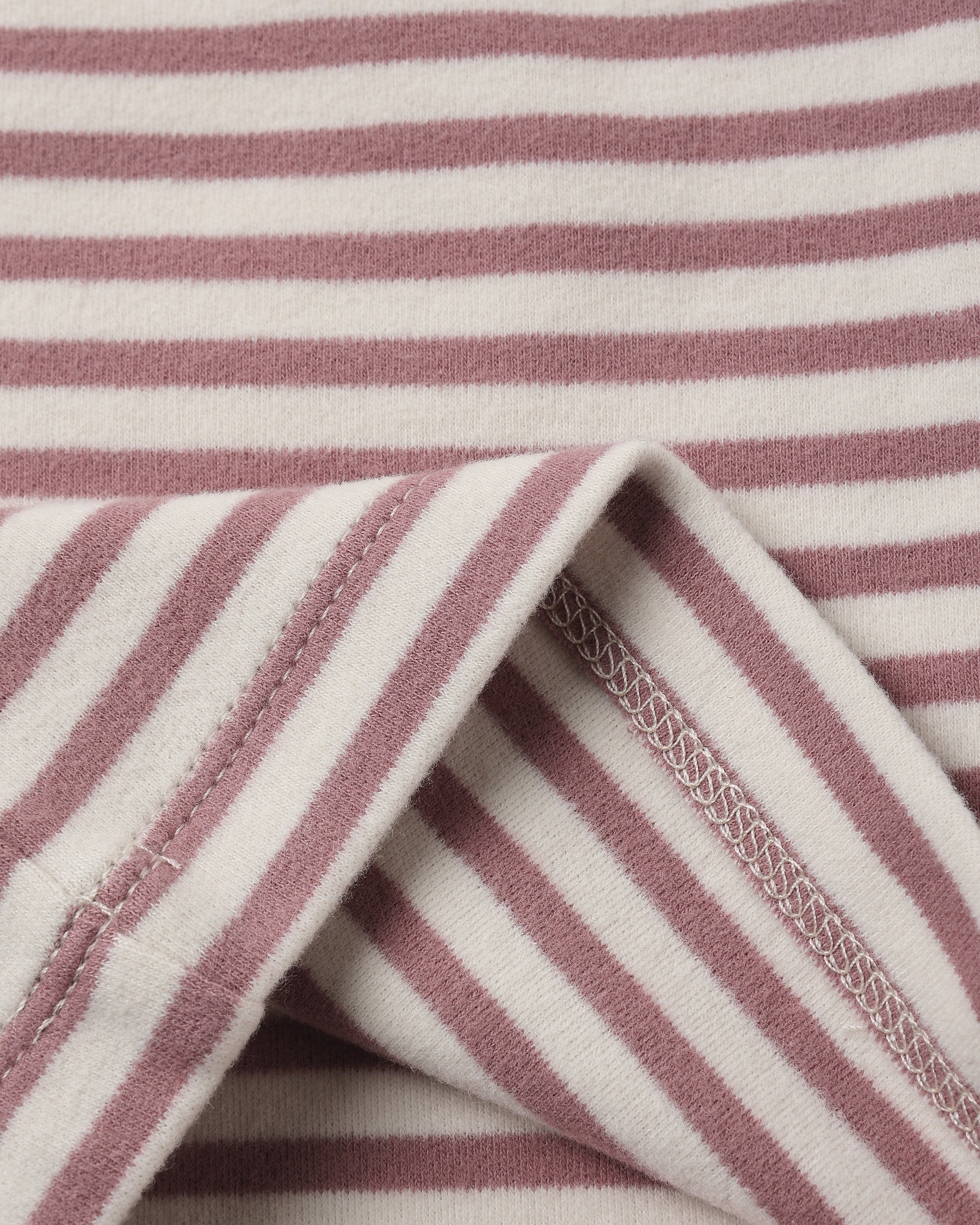 Close-up of a striped fabric with alternating dusty rose and off-white horizontal stripes, showing a folded corner with stitched edges.