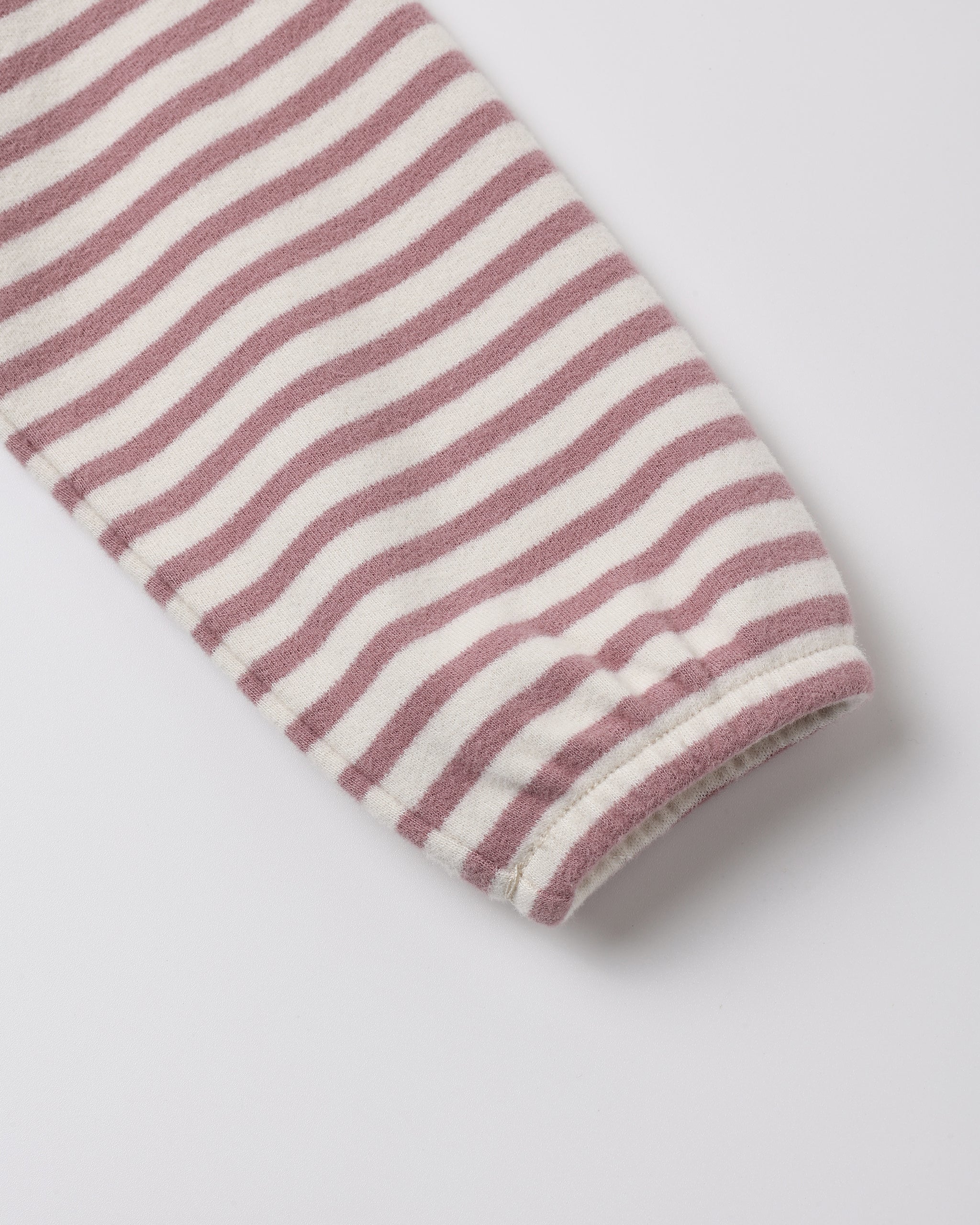 A close-up of a striped fabric sleeve or cuff with alternating dusty rose and off-white horizontal stripes, finished with a ribbed hem, on a light gray background.