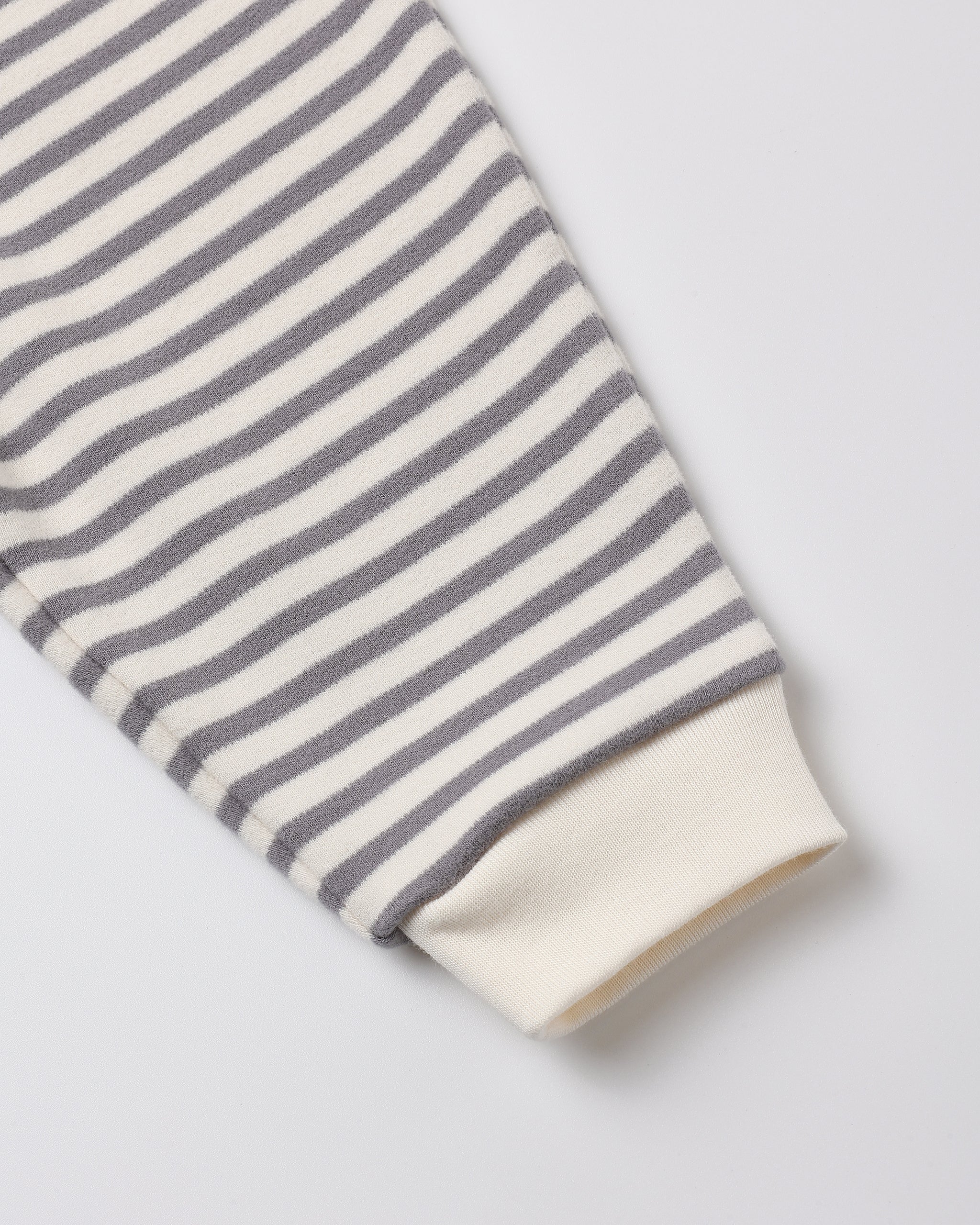 A close-up of a striped knit sleeve with alternating gray and off-white horizontal stripes, finished with an off-white ribbed cuff, shown on a light gray background.
