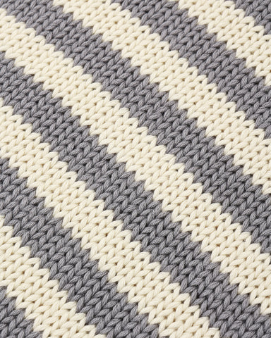 Close-up of a knitted fabric with diagonal stripes in warm off-white and medium gray.