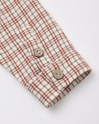 Close-up of a plaid shirt sleeve with a cream base, rust red and gray check pattern, and two wooden buttons on a white background.