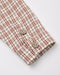 Close-up of a plaid shirt sleeve with a cream base, rust red and gray check pattern, and two wooden buttons on a white background.