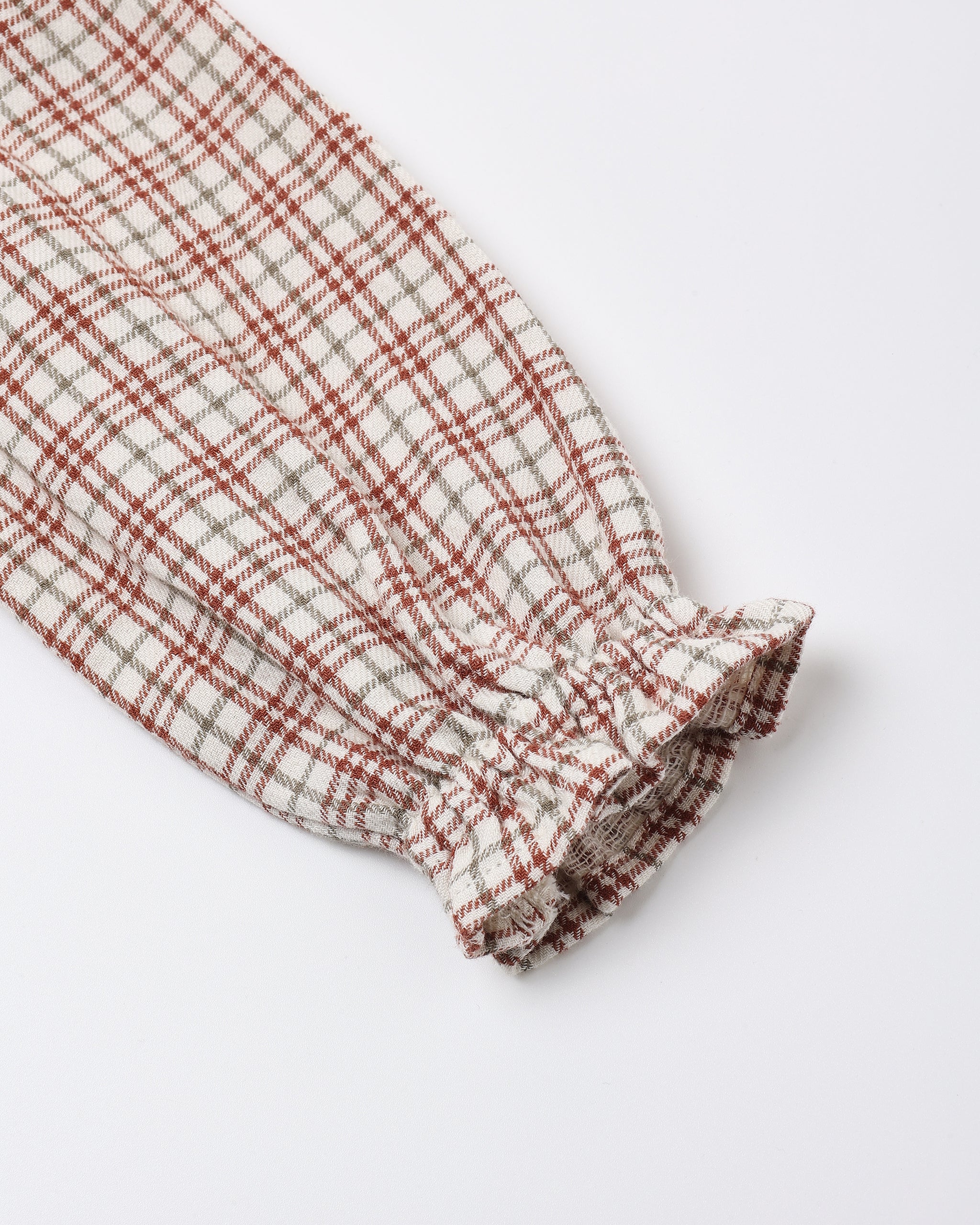A close-up of a textured fabric sleeve with a gathered elastic cuff, featuring a plaid pattern in rust red, beige, and gray on a white background.