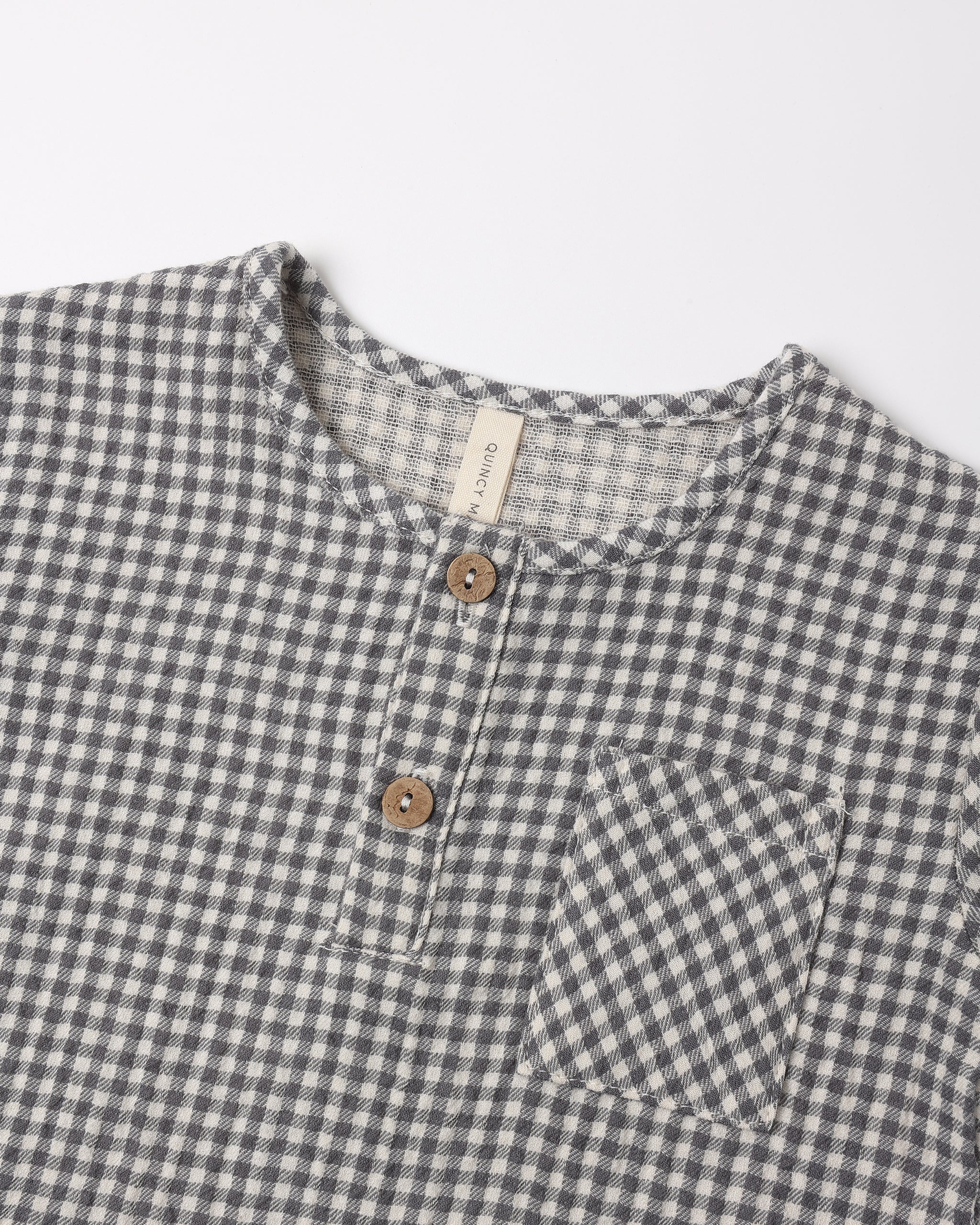A close up of the woven black gingham fabric with a front two-button placket and chest pocket